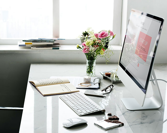 desk with computer monitor and flowers near window